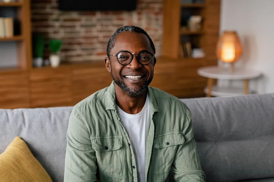 Andropause-Doctor A middle aged black man in a green button up shirt sits on his couch smiling, happy with his treatment for andropause and low testosterone from Balanced Medical Solutions in San Francisco Bay Area.