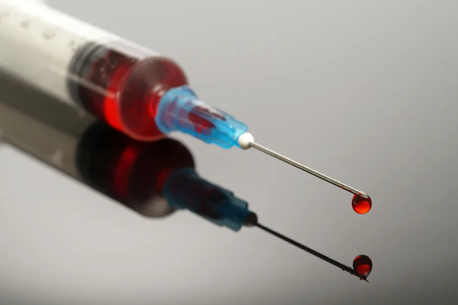 A close-up of a medical syringe filled with a red liquid, capturing a drop of the liquid falling from the needle. Lipo-B12 Weight Loss Injecitons offered by Balanced Medical Solutions in San Francisco Bay Area.