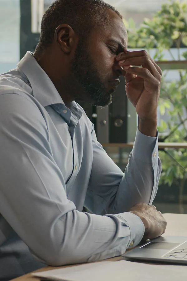 A black man rubbing the top of his nose at his desk, in need of chronic fatigue treatment from Balanced Medical Solutions in San Francisco Bay Area.
