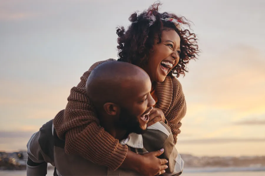 A black couple playfully piggybacking at sunset. Schedule Hi-EMT Chair pelvic floor therapy from Balanced Medical Solutions in San Francisco Bay Area.
