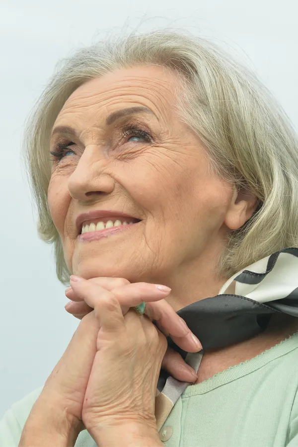 An older woman holds her hands together under her chin and looks up at a cool sky smiling. Get treatment for hot flashes and night sweats from Balanced Medical Solutions in San Francisco Bay Area.