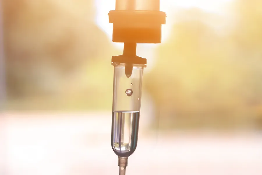 Close-up of an IV drip warmly lit by a window showing trees and a sunset, representing IV therapy from Balanced Medical Solutions in San Francisco Bay Area.