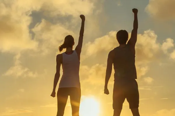 A couple raise their right arms in the air in triumph, framed by the sunrise. Get Ipamorelin peptide treatment from Balanced Medical Solutions in San Francisco Bay Area.