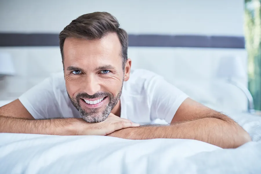 A middle-aged man lays on his stomach in bed smiling. Schedule treatment for low libido in men from Balanced Medical Solutions in San Francisco Bay Area.