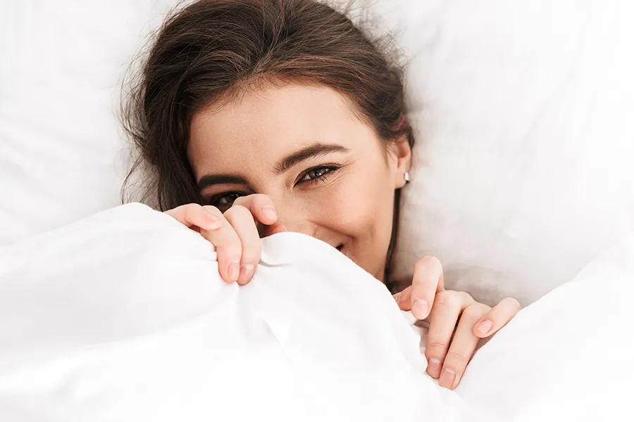 A woman smiling and laying in bed. Schedule medications for painful intercourse from Balanced Medical Solutions in San Francisco Bay Area.