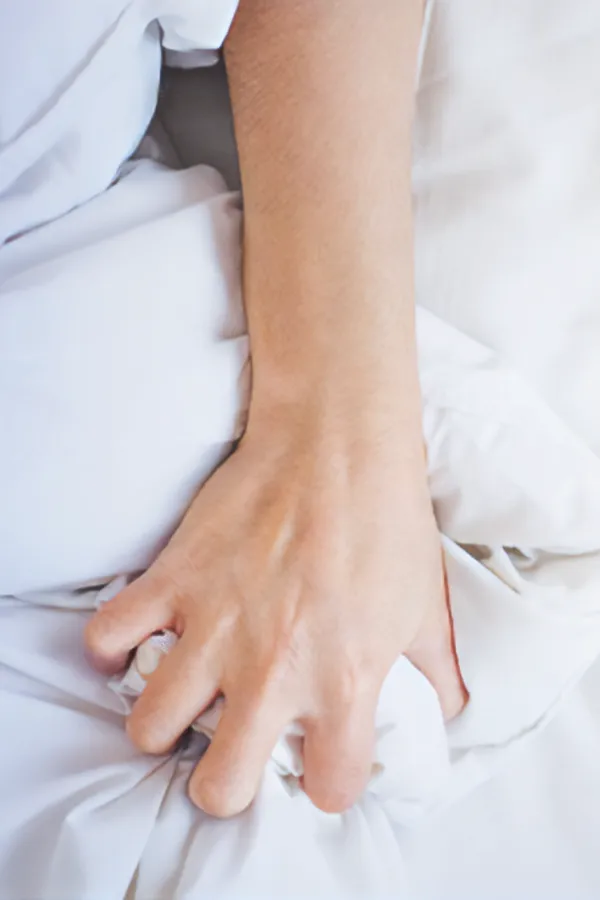 Close-up of a woman's hand gripping sheets on a bed. Get medications for painful intercourse from Balanced Medical Solutions in San Francisco Bay Area.