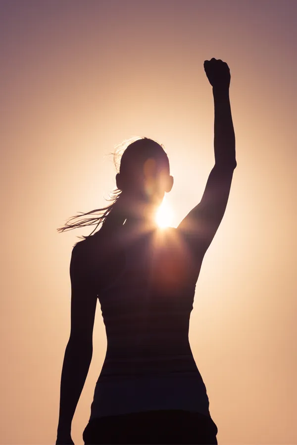 A woman raises her fist in the air, silhouetted by the sun. Get methylene blue IV therapy from Balanced Medical Solutions in San Francisco Bay Area.