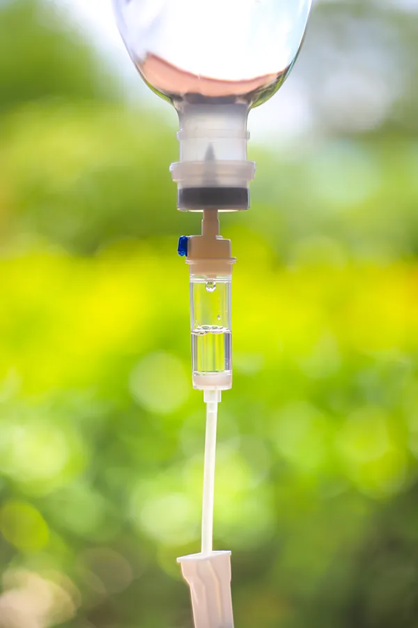 Close-up of an IV drip against a forest background. Get the Myers Cocktail IV treatment from Balanced Medical Solutions in San Francisco Bay Area.