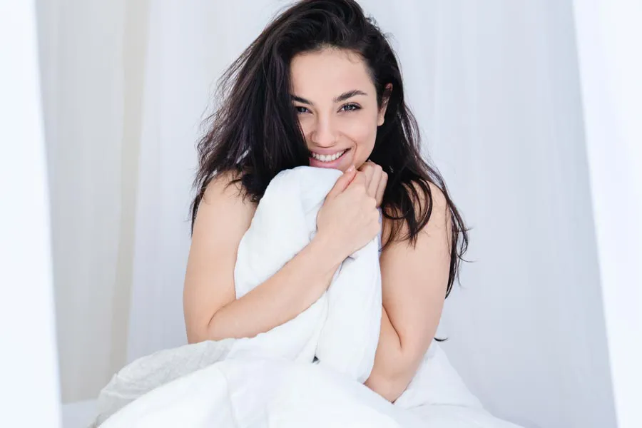 Oxytocin-for-Female-Sexual-Enhancement-Clinic A joyful young woman with dark hair, smiling broadly and holding a white towel close to her chest, satisfied with the results of Oxytocin for Female Sexual Enhancement treatment offered by Balanced Medical Solutions in San Francisco Bay Area.