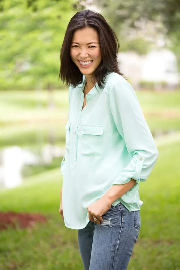A middle-aged brunette woman in a light green button-up shirt stands outside smiling, happy with her perimenopause treatment from Balanced Medical Solutions in San Francisco Bay Area.