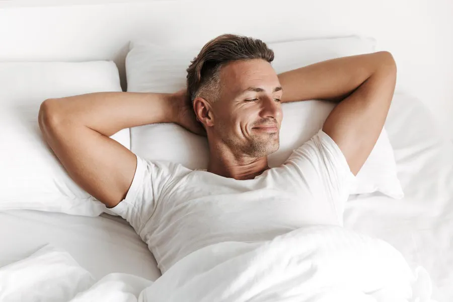 A smiling man lays in bed with his hands behind his head. Get treatment for Peyronies Disease from Balanced Medical Solutions in San Francisco Bay Area.