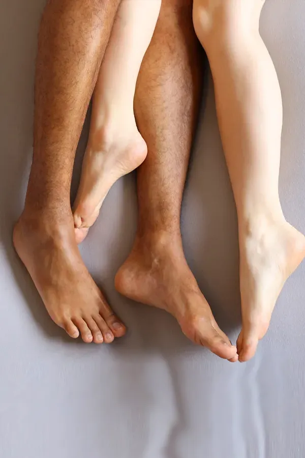 Photo from the knees to the feet of a couples nude legs entwined on a bed, representing shockwave treatment for erectile dysfunction from Balanced Medical Solutions in San Francisco Bay Area.