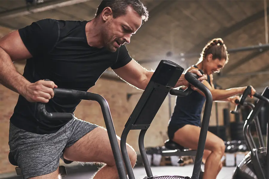A couple in a brick gym work as hard as they can on exercise bikes, inspired by successful Tirzepatide treatment from Balanced Medical Solutions in San Francisco Bay Area.