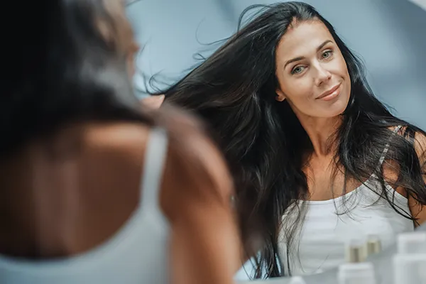 A woman looks at her long, black, healthy hair in the mirror. Get stem cells and exosomes for hair restoration from Balanced Medical Solutions in San Francisco Bay Area.